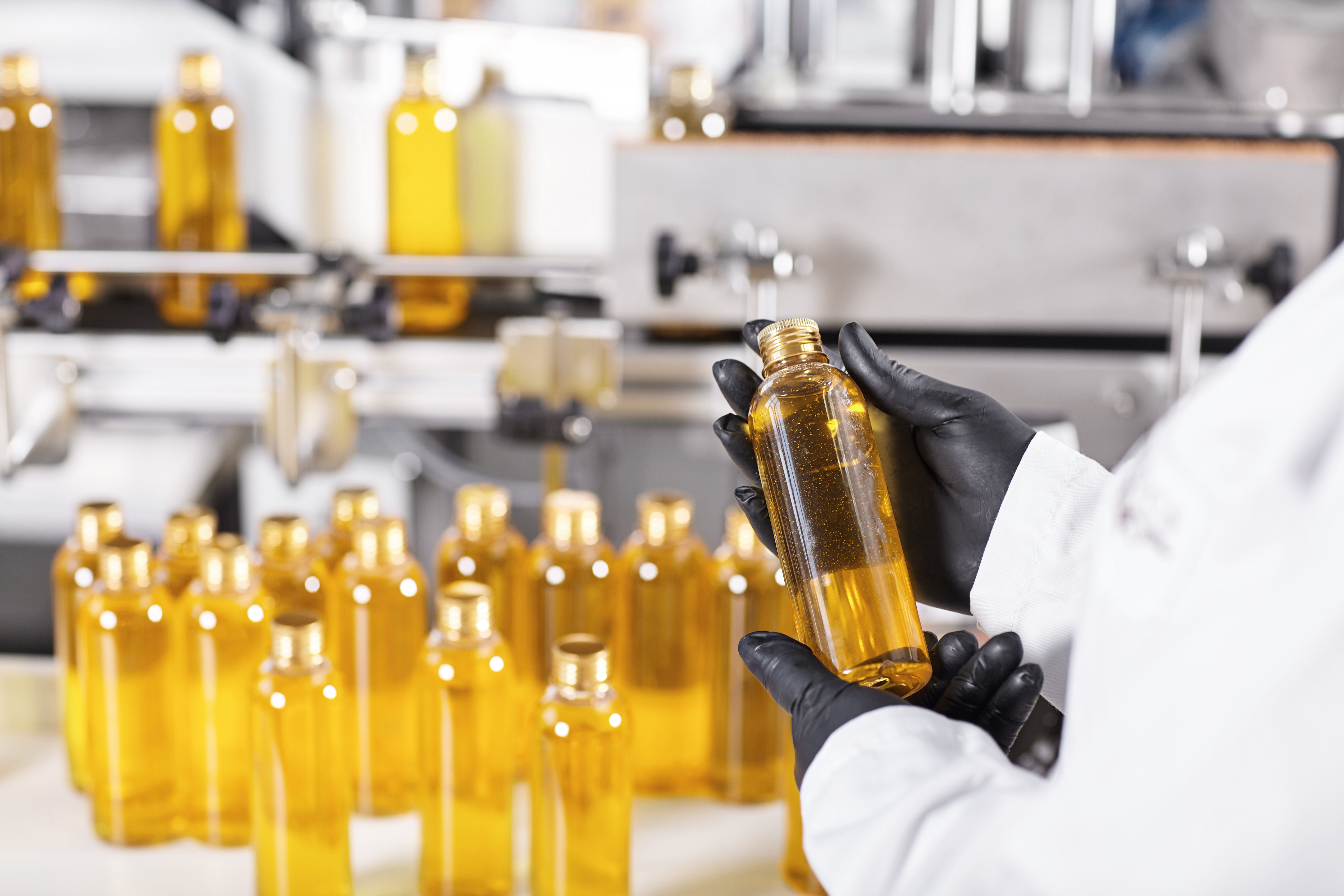 Medical production, pharmacy and healthcare industry. Employee wearing protective clothes holding bottle with golden substance in his hands, conducting quality control of end product at factory